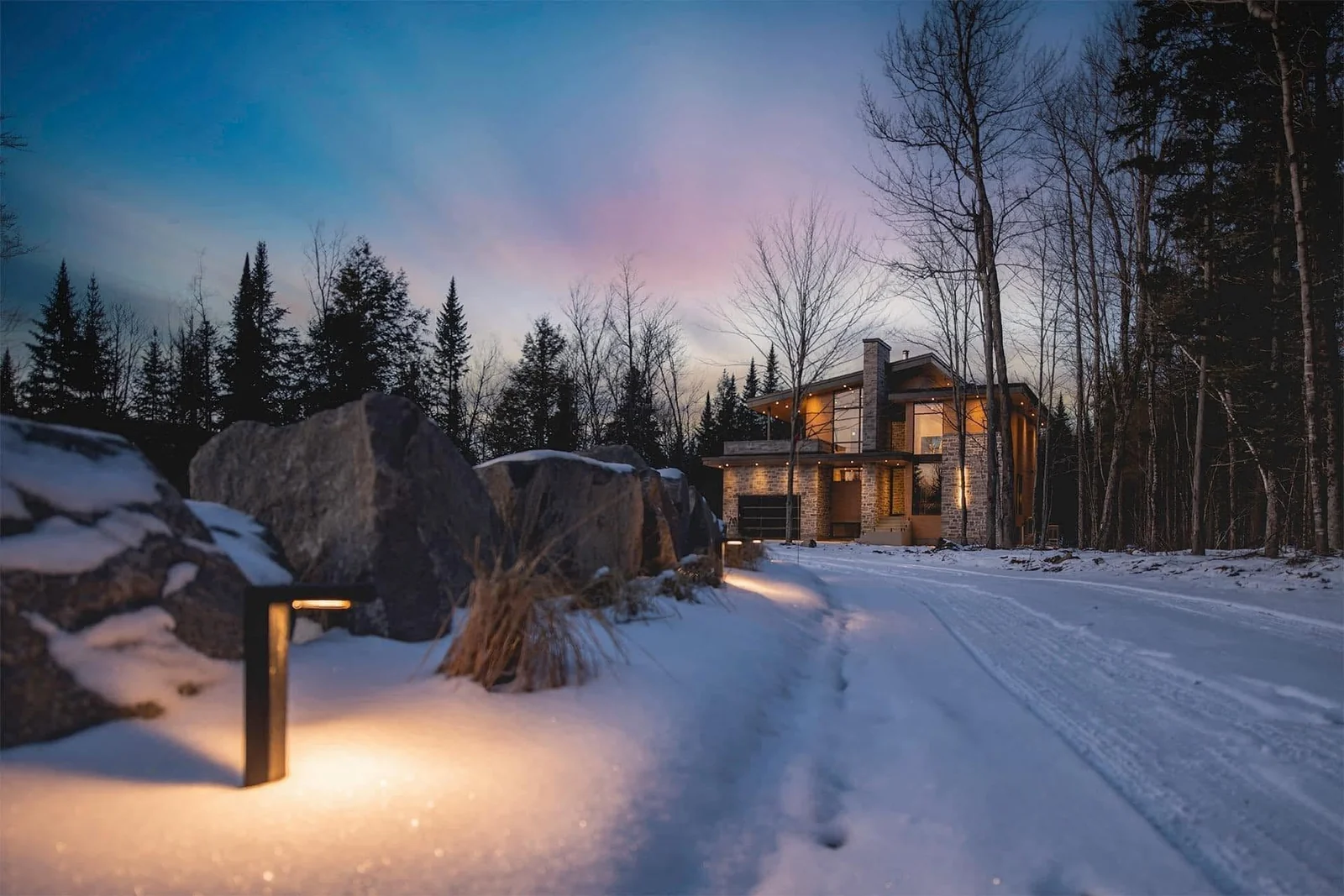 Chalet éclairé dans un paysage boisé et enneigé au crépuscule