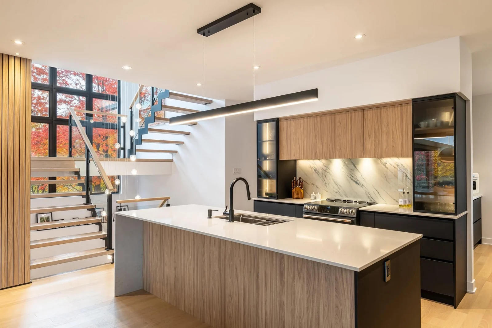 Cuisine avec îlot en bois, escalier suspendu et grandes fenêtres